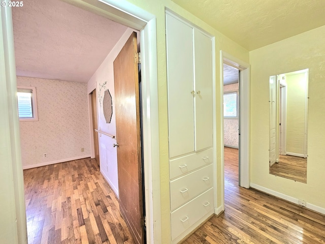 corridor featuring a textured ceiling, plenty of natural light, and wood finished floors
