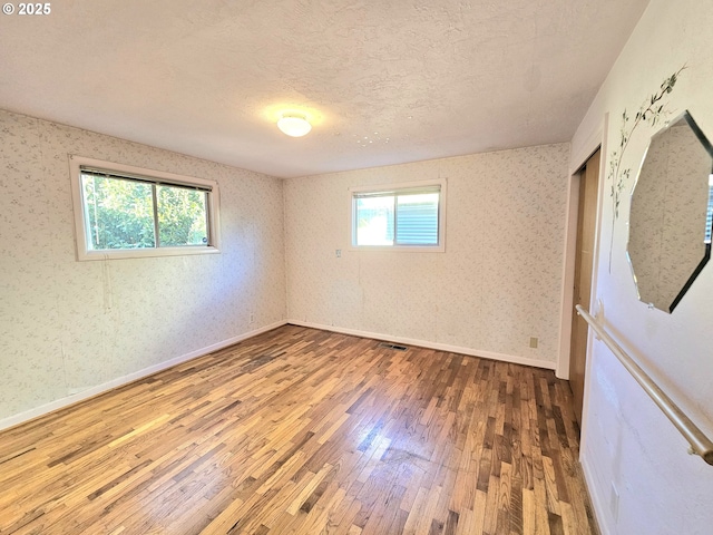 spare room featuring a textured ceiling, baseboards, wallpapered walls, and wood finished floors