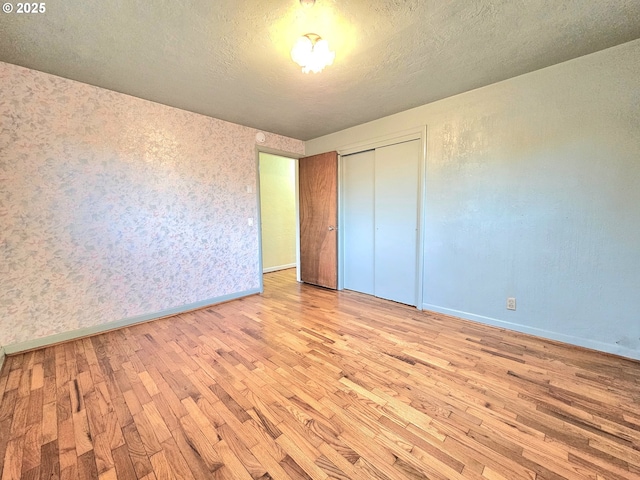 unfurnished bedroom featuring a closet, baseboards, a textured ceiling, and hardwood / wood-style floors
