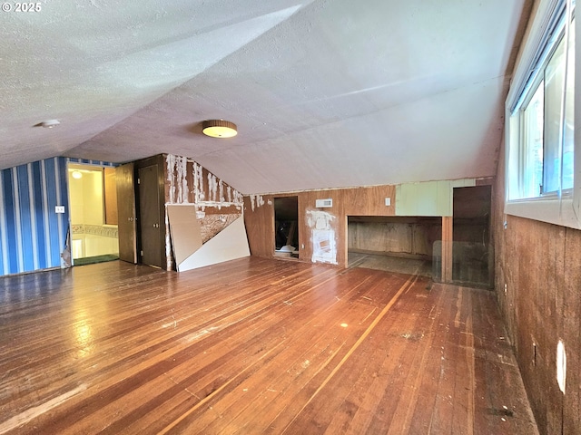 unfurnished living room with a textured ceiling, wood walls, hardwood / wood-style floors, and lofted ceiling