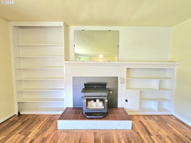 interior details featuring a wood stove, wood finished floors, baseboards, a textured ceiling, and built in shelves