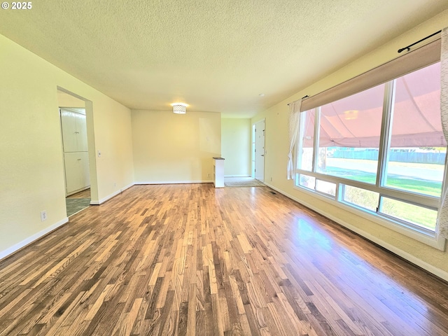 unfurnished living room with baseboards, a textured ceiling, and wood finished floors