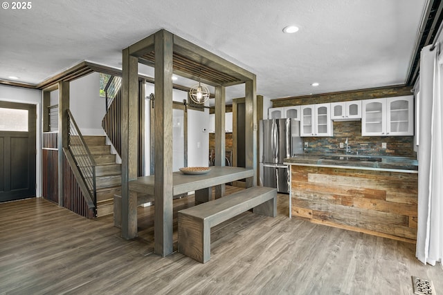 kitchen featuring freestanding refrigerator, backsplash, glass insert cabinets, wood finished floors, and a textured ceiling
