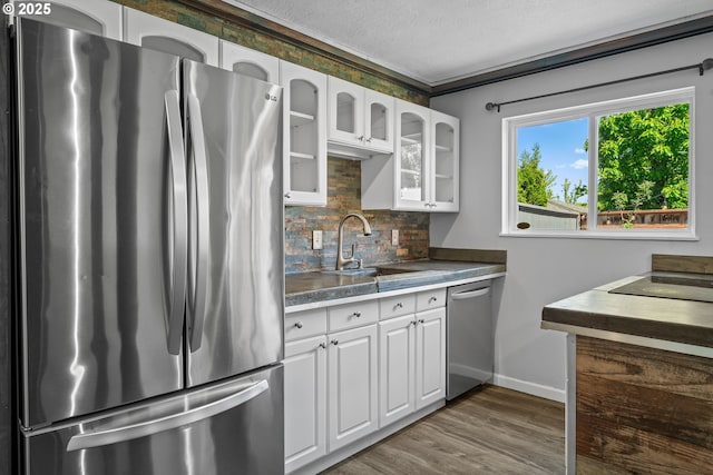 kitchen with appliances with stainless steel finishes, decorative backsplash, white cabinets, glass insert cabinets, and wood finished floors