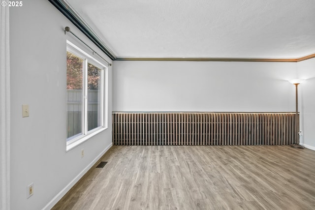 spare room with wood finished floors, a textured ceiling, ornamental molding, and baseboards