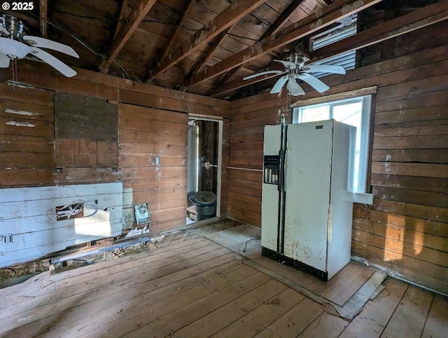 interior space featuring wood walls, white refrigerator with ice dispenser, a ceiling fan, and wood finished floors