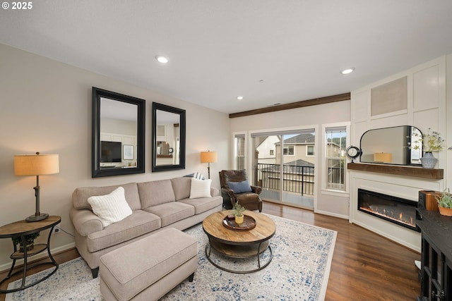 living area with baseboards, dark wood-style flooring, a glass covered fireplace, and recessed lighting