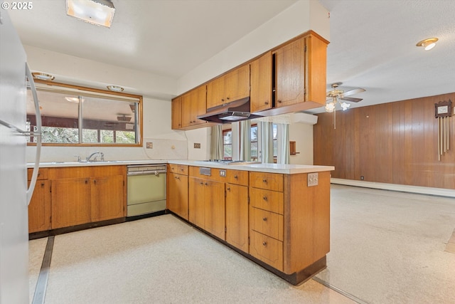 kitchen featuring brown cabinetry, a peninsula, freestanding refrigerator, under cabinet range hood, and dishwasher