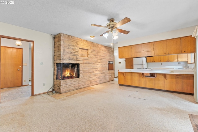 kitchen with a textured ceiling, freestanding refrigerator, a stone fireplace, light countertops, and ceiling fan