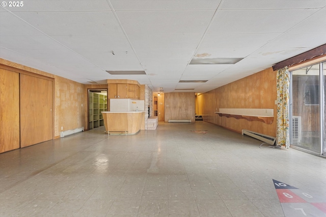 basement featuring a baseboard heating unit, wood walls, light floors, baseboard heating, and a paneled ceiling