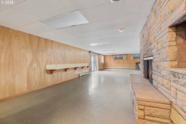 basement featuring a baseboard heating unit, wood walls, a fireplace, tile patterned floors, and a paneled ceiling