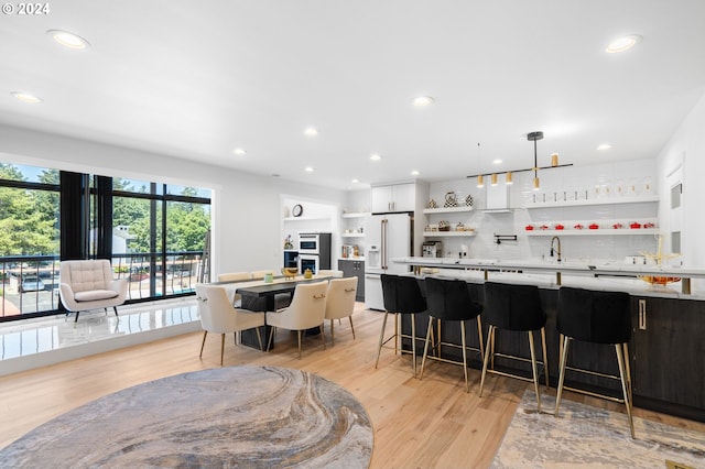 kitchen featuring white cabinetry, white fridge with ice dispenser, hanging light fixtures, tasteful backsplash, and a kitchen bar