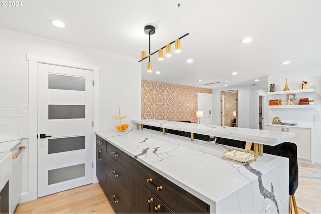 kitchen with light stone counters, a breakfast bar, hanging light fixtures, and light hardwood / wood-style floors