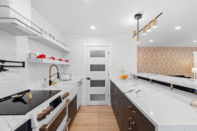 kitchen featuring decorative light fixtures, light stone counters, light wood-type flooring, and high end stainless steel range