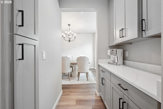 kitchen with an inviting chandelier, baseboards, light stone countertops, and light wood-style flooring