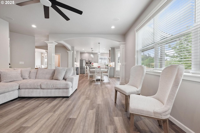 living room featuring a ceiling fan, decorative columns, arched walkways, recessed lighting, and light wood-style flooring
