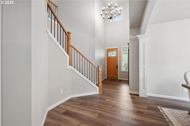 entrance foyer with wood finished floors, stairway, baseboards, an inviting chandelier, and a high ceiling