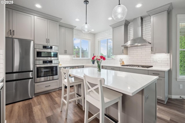 kitchen featuring dark wood-style flooring, gray cabinets, wall chimney exhaust hood, tasteful backsplash, and appliances with stainless steel finishes
