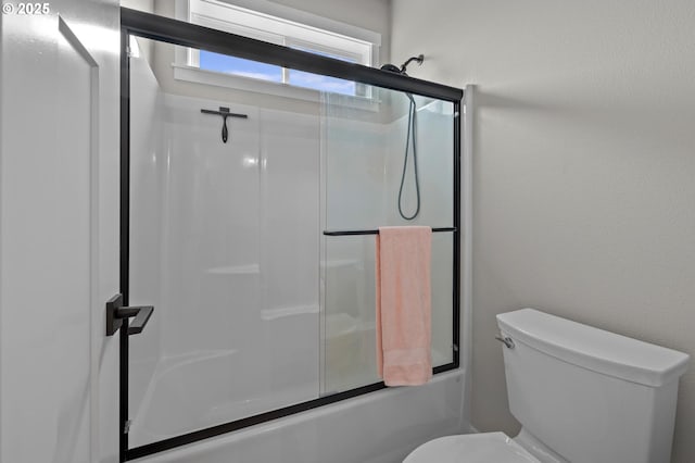 bathroom featuring toilet and bath / shower combo with glass door