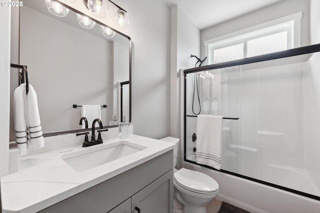 full bathroom featuring vanity, combined bath / shower with glass door, and toilet