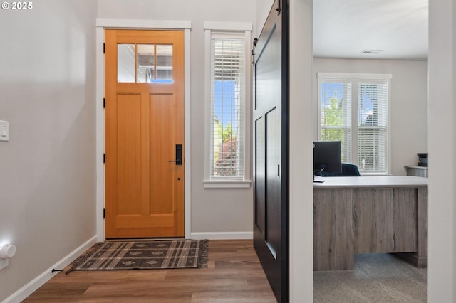 foyer entrance with baseboards, visible vents, a barn door, and wood finished floors