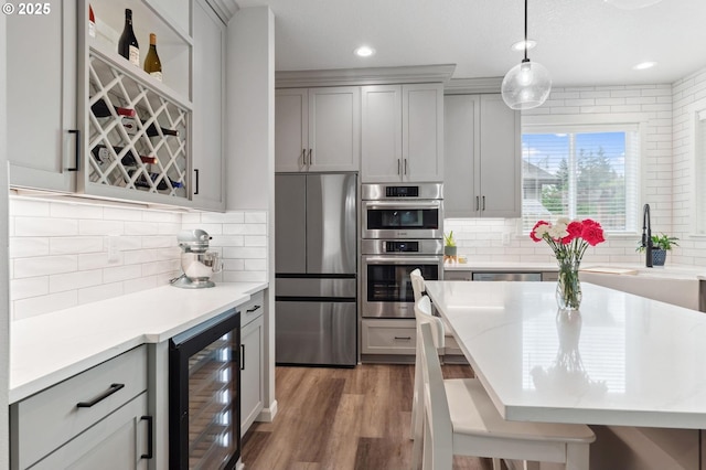 kitchen with beverage cooler, decorative backsplash, appliances with stainless steel finishes, and wood finished floors