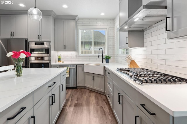 kitchen featuring wall chimney range hood, appliances with stainless steel finishes, a sink, gray cabinets, and wood finished floors