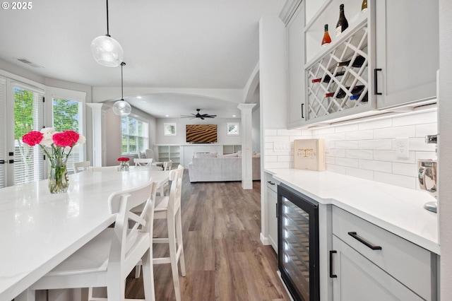 bar with ceiling fan, decorative backsplash, a dry bar, wood finished floors, and beverage cooler
