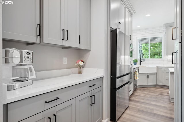 kitchen featuring decorative backsplash, freestanding refrigerator, light stone countertops, a sink, and light wood-style flooring