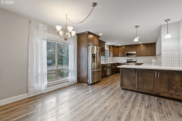 kitchen featuring sink, decorative light fixtures, light hardwood / wood-style flooring, kitchen peninsula, and stainless steel appliances