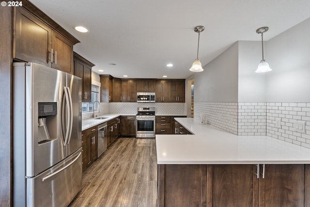 kitchen with pendant lighting, sink, dark brown cabinetry, kitchen peninsula, and stainless steel appliances