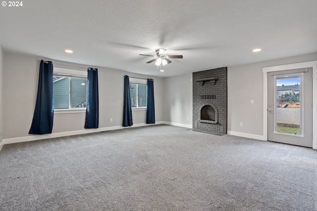 unfurnished living room with ceiling fan, carpet floors, a brick fireplace, and a textured ceiling