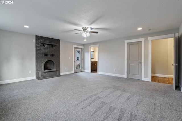 unfurnished living room featuring a brick fireplace, ceiling fan, a textured ceiling, and carpet flooring