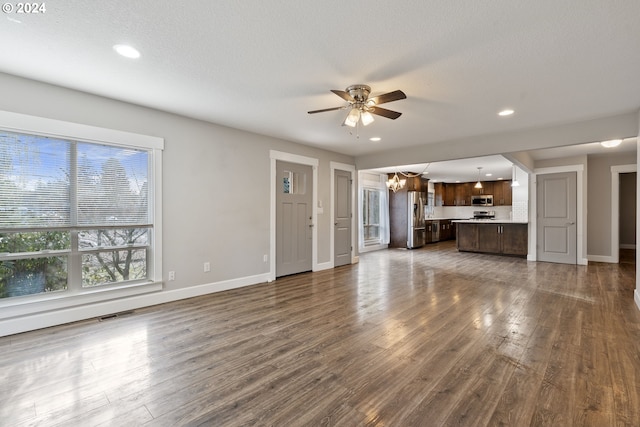 unfurnished living room with ceiling fan with notable chandelier, a textured ceiling, and dark hardwood / wood-style flooring