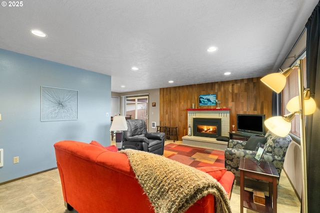 living room with wooden walls, a brick fireplace, and a textured ceiling