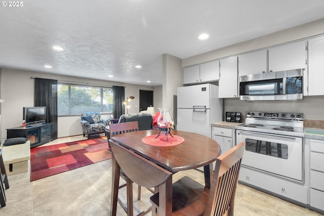 kitchen with a textured ceiling, white cabinets, white appliances, and light tile patterned floors