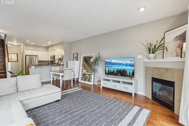 living room with a tiled fireplace, wood finished floors, recessed lighting, stairway, and baseboards