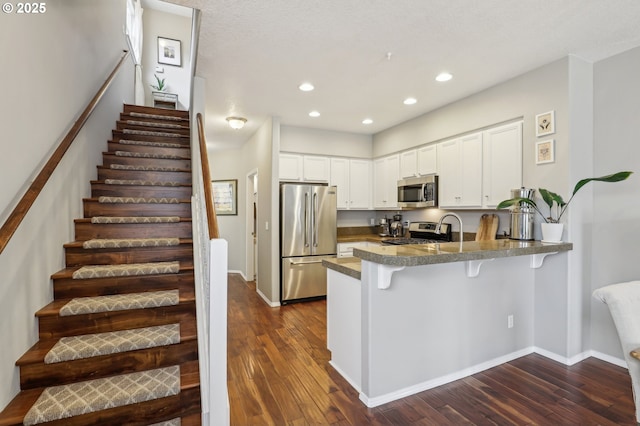 kitchen featuring dark wood-type flooring, a kitchen breakfast bar, stainless steel appliances, a peninsula, and white cabinets