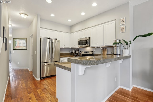 kitchen featuring dark wood finished floors, tile countertops, appliances with stainless steel finishes, a peninsula, and white cabinets