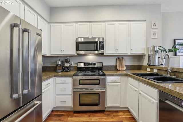 kitchen with dark wood-style flooring, a sink, stainless steel appliances, tile counters, and white cabinets