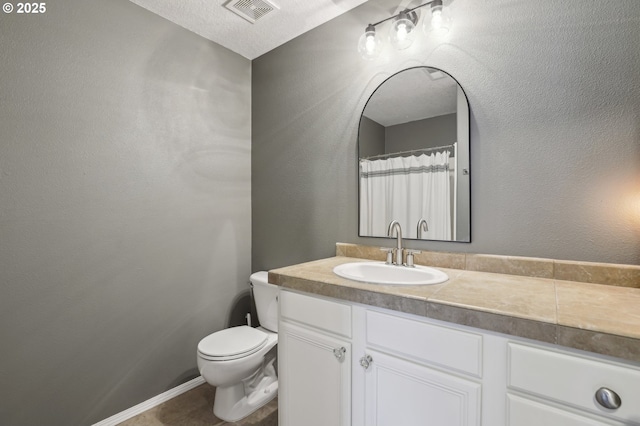 bathroom with vanity, toilet, a textured wall, and visible vents