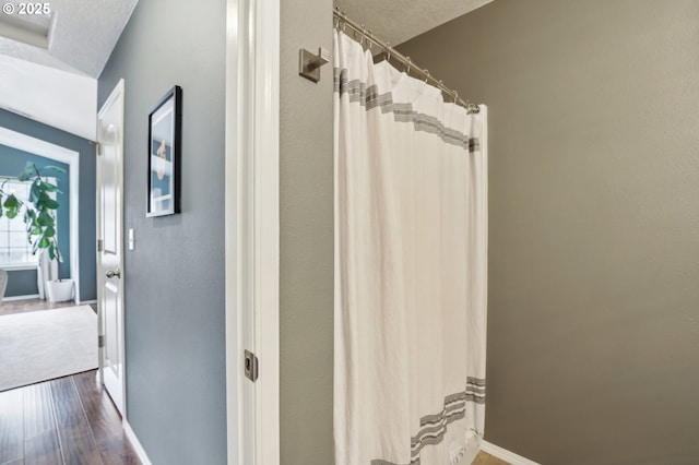 full bathroom featuring curtained shower, wood finished floors, baseboards, and a textured ceiling