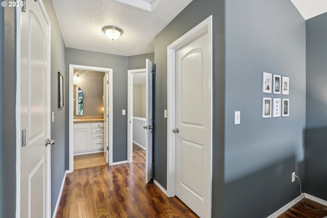 hallway featuring baseboards, dark wood-type flooring, and a textured ceiling