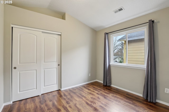 unfurnished bedroom with visible vents, baseboards, a closet, lofted ceiling, and dark wood-style floors