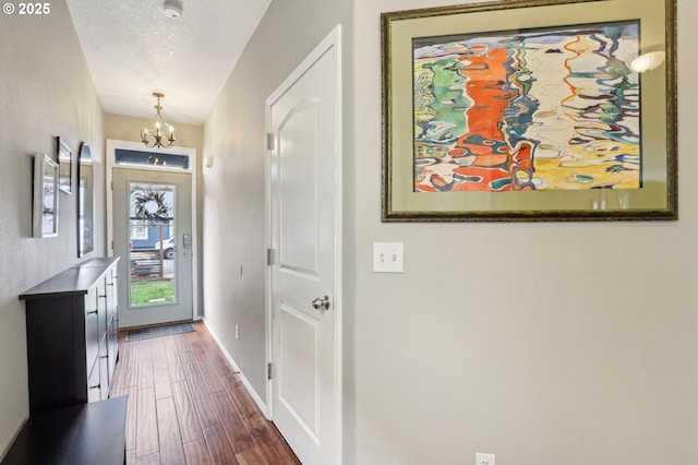 foyer entrance featuring baseboards, dark wood-type flooring, an inviting chandelier, and a textured ceiling