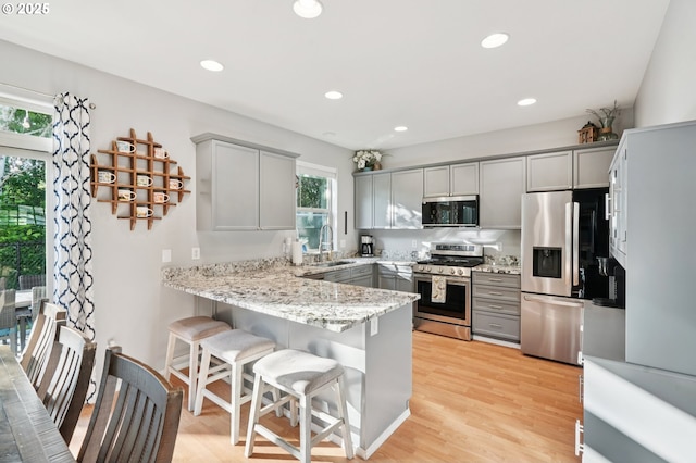 2149 SE Williams Dr, Gresham, OR 97080 - kitchen with appliances with stainless steel finishes, gray cabinets, a peninsula, light stone counters, and a breakfast bar area