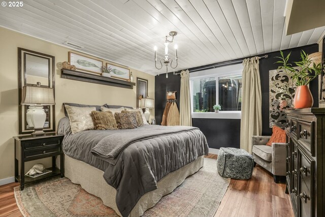 bedroom with an inviting chandelier, visible vents, wood finished floors, baseboards, and wooden ceiling