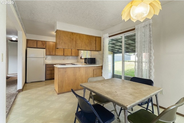 kitchen featuring white refrigerator, decorative backsplash, kitchen peninsula, and a textured ceiling