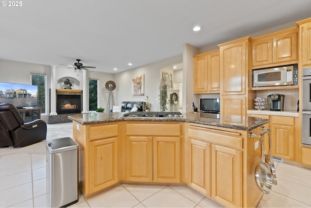 kitchen featuring ceiling fan, light brown cabinets, stainless steel appliances, open floor plan, and a glass covered fireplace