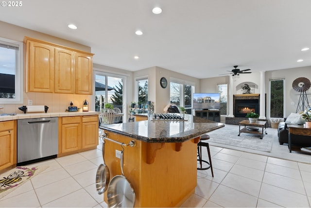 kitchen with a warm lit fireplace, light tile patterned flooring, stainless steel appliances, a breakfast bar, and open floor plan